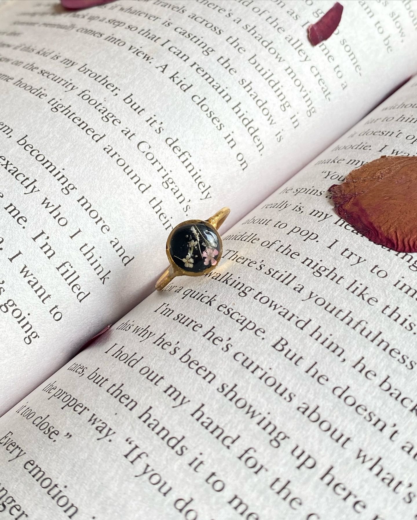 The ring alone on the open page, small against the printed text, with a red petal beside it