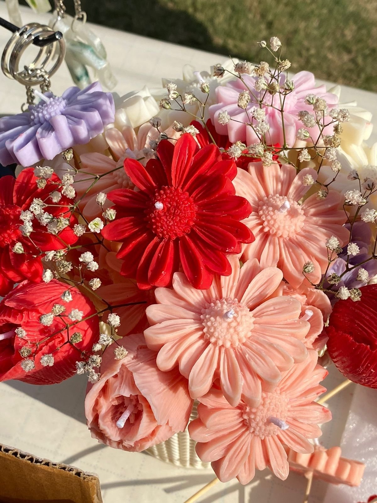 A bouquet of wax flowers in red, coral, pink and cream, arranged with sprays of dried gypsophila