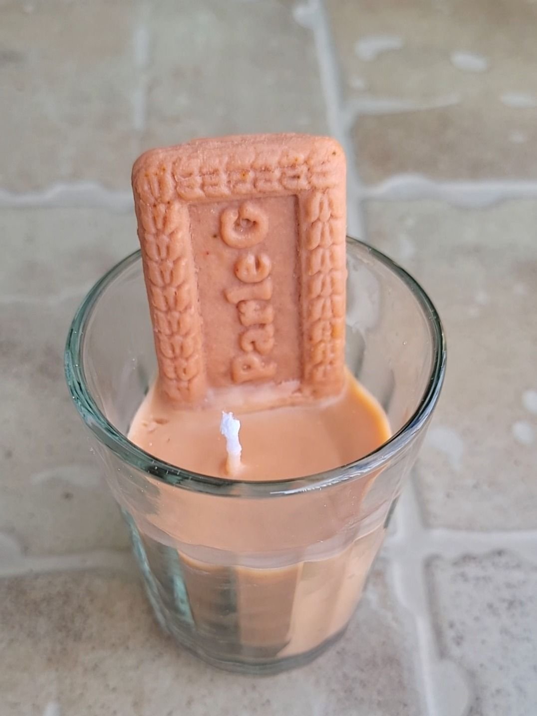 A candle poured to look like a glass of chai with a biscuit resting on the rim