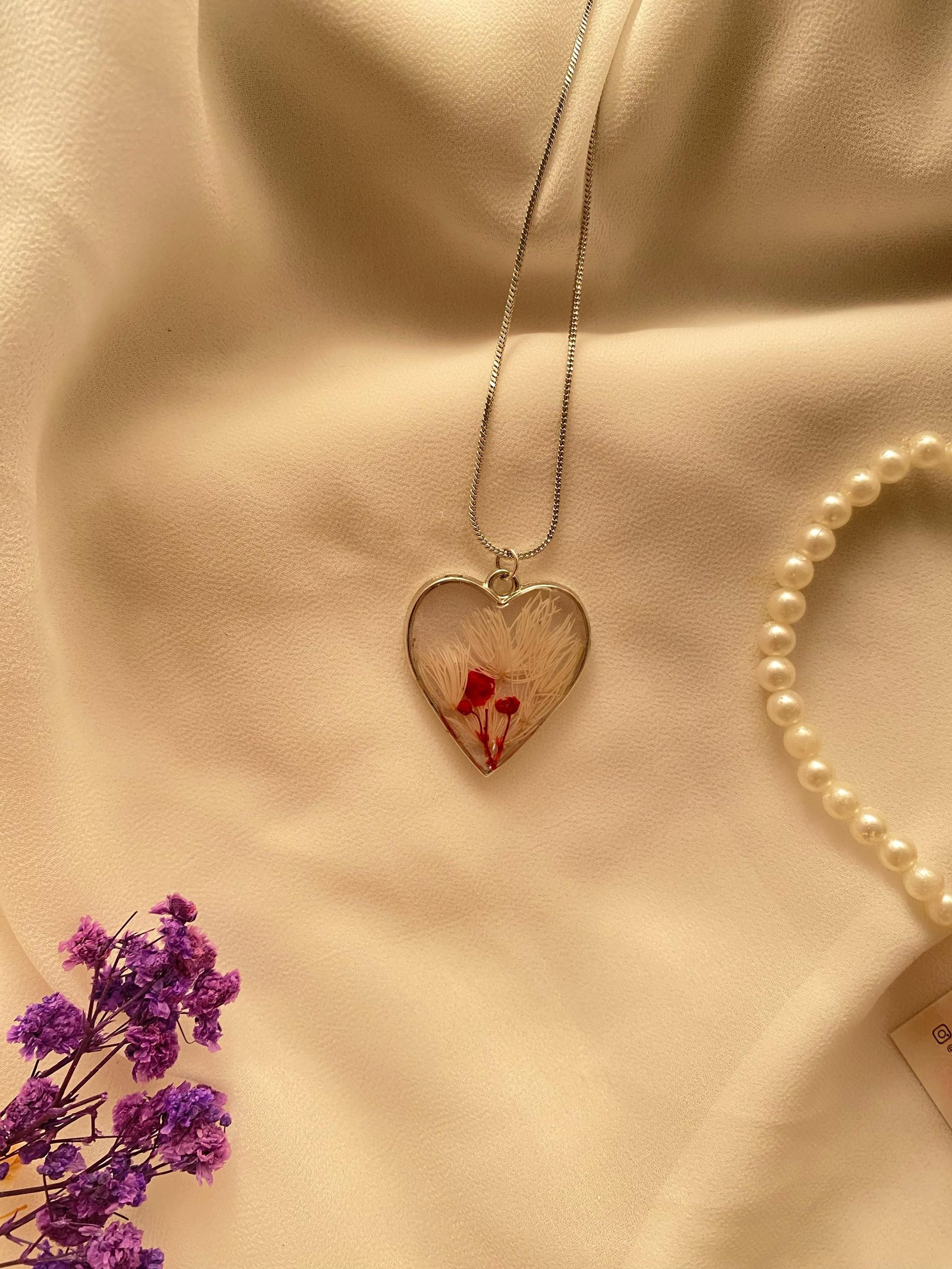 A silver heart holding a smaller red bloom, photographed with pearls and dried lilac