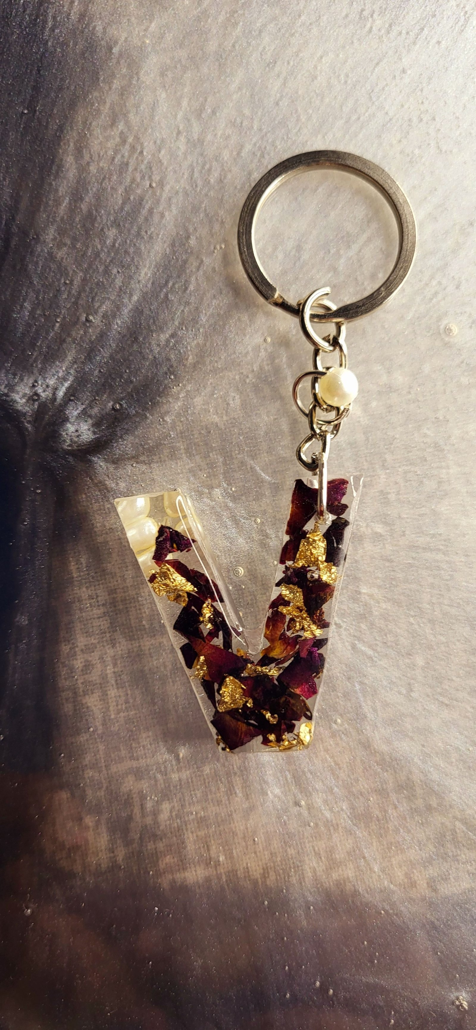 An initial keychain set with rose petals and gold leaf, held against dark fabric