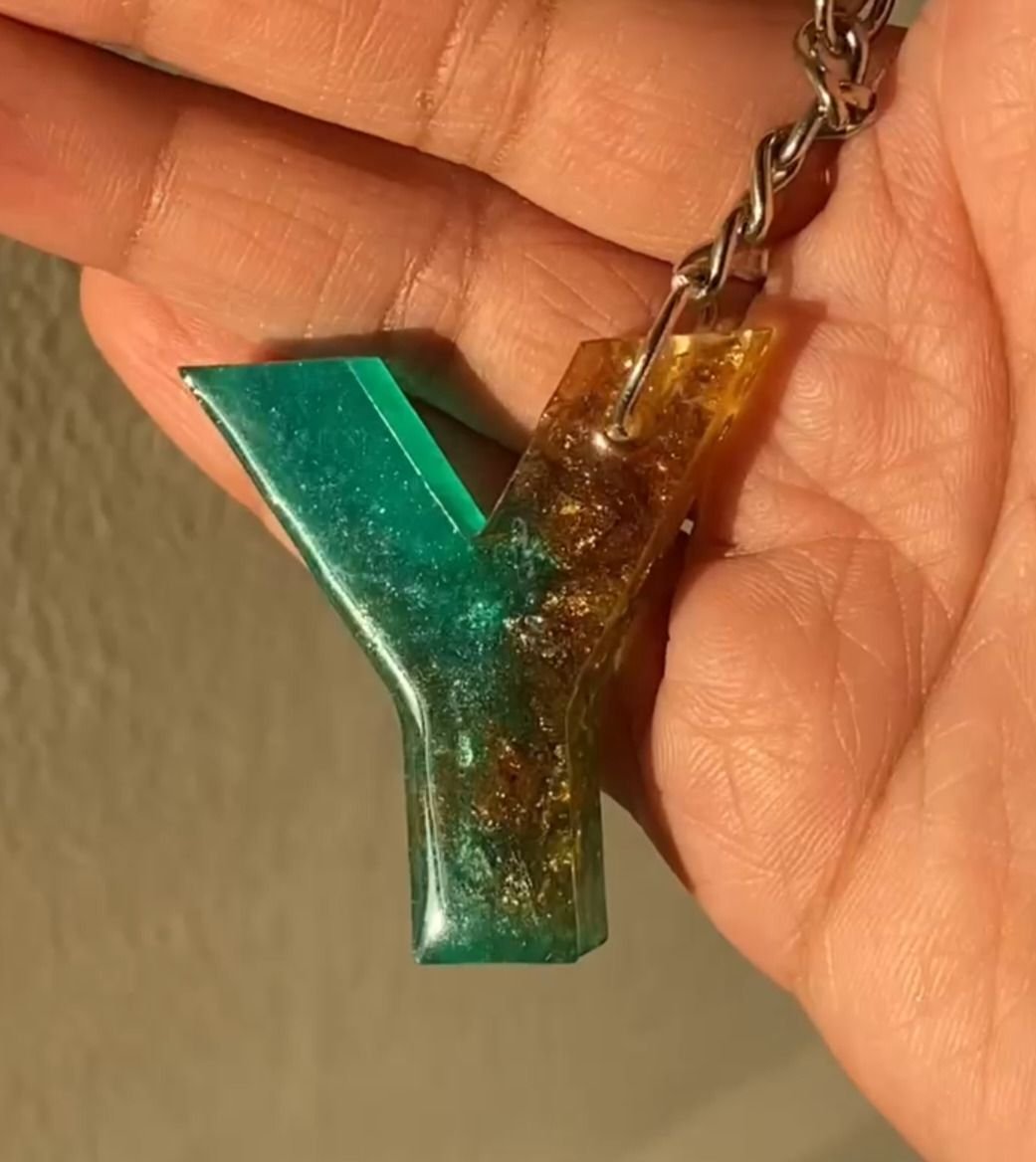 A resin initial Y in green shading into amber, flecked with gold, on a silver chain and held in the hand
