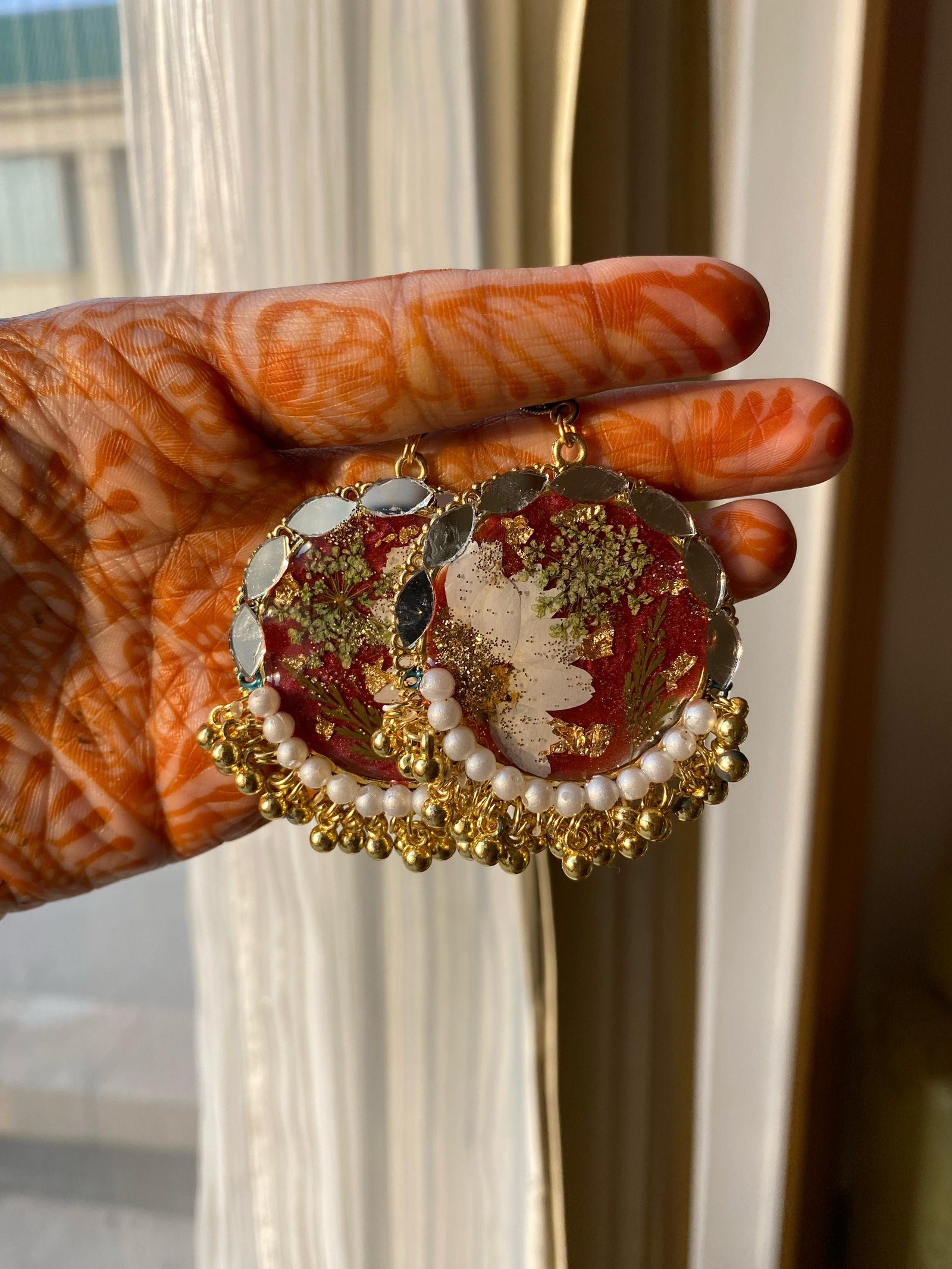 A closely related pair in red and white with freshwater pearls, held in a hand patterned with henna