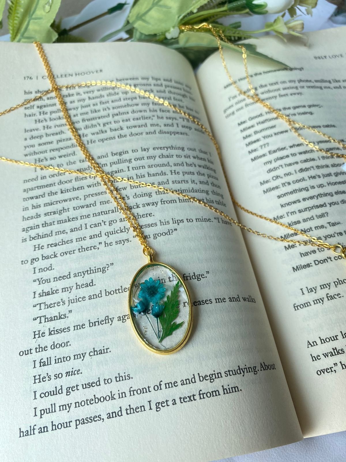 An oval pendant holding a blue flower, photographed on the pages of an open book