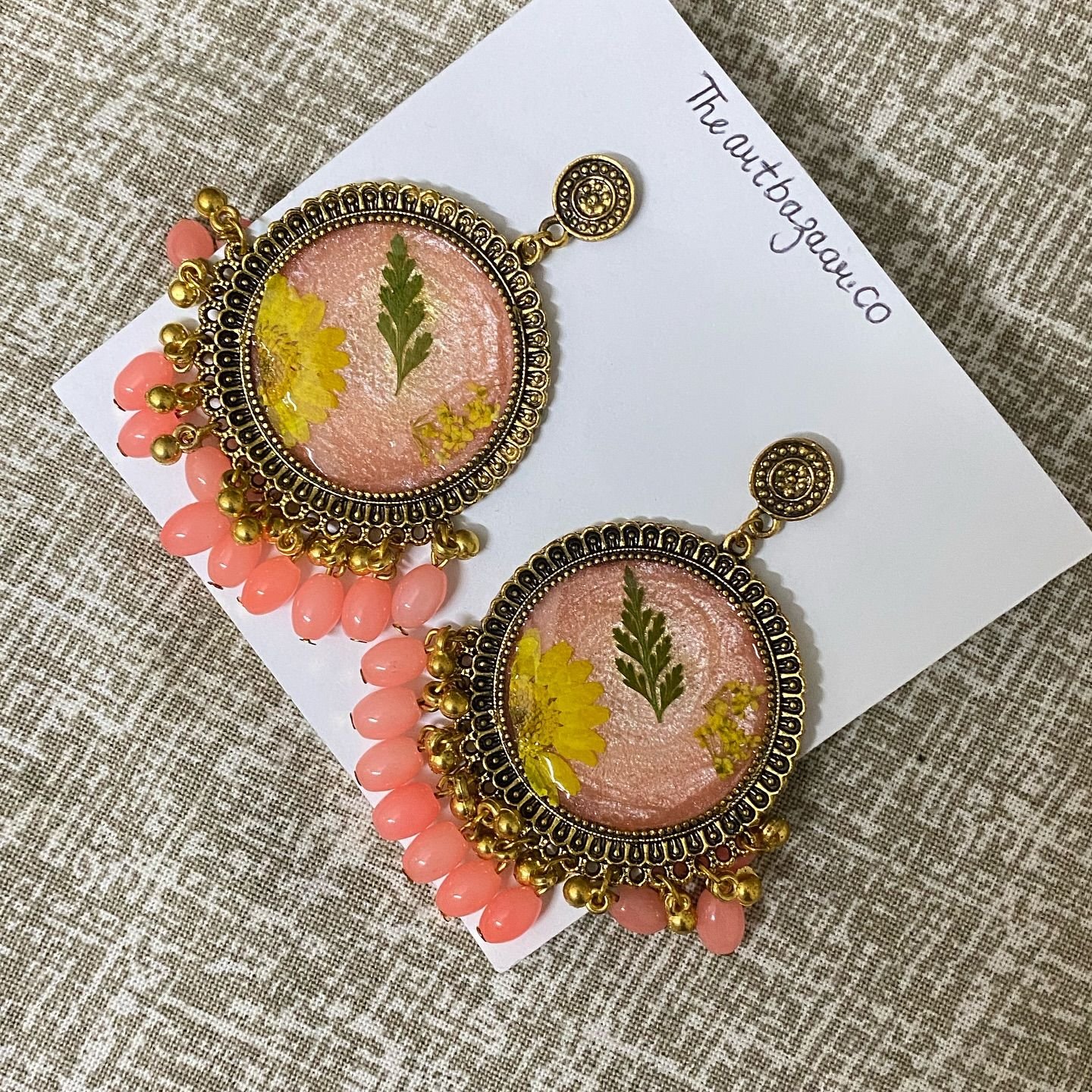 The same pair laid on the card against textured cream fabric, showing the petals through the resin