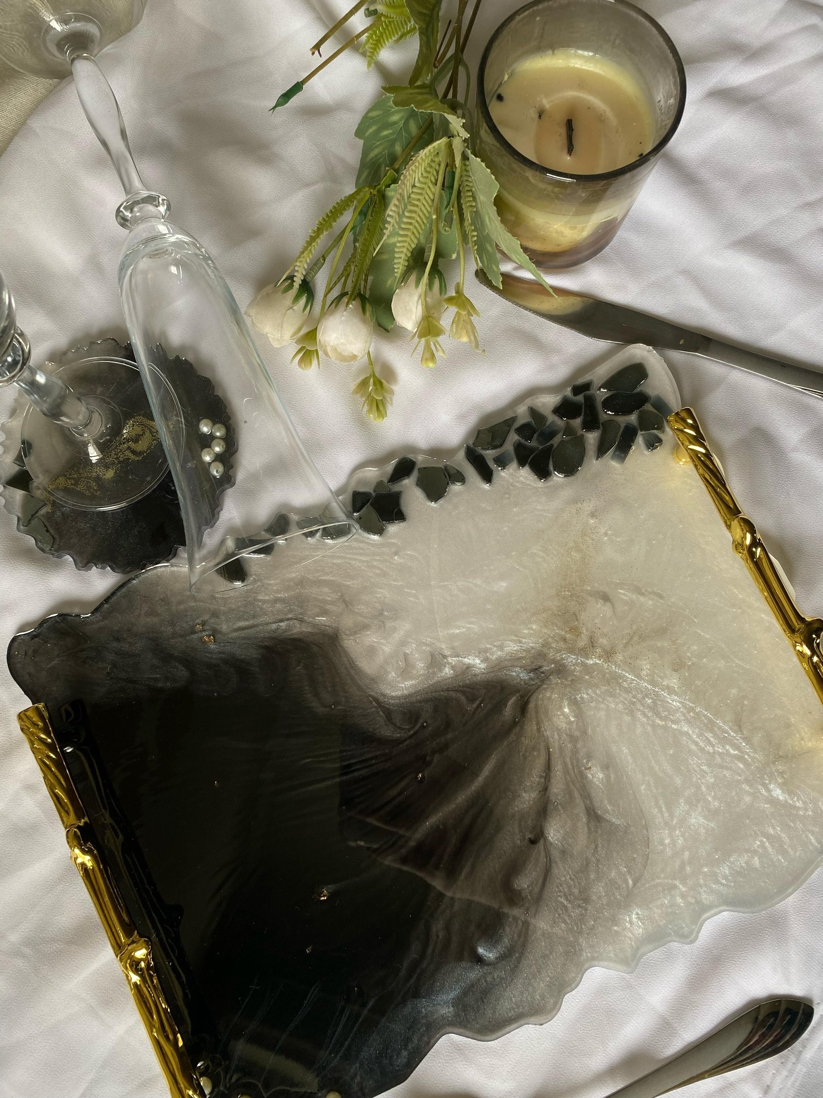 A large rectangular tray poured in swirled black and white resin with slim gold handles, photographed with white flowers and a candle