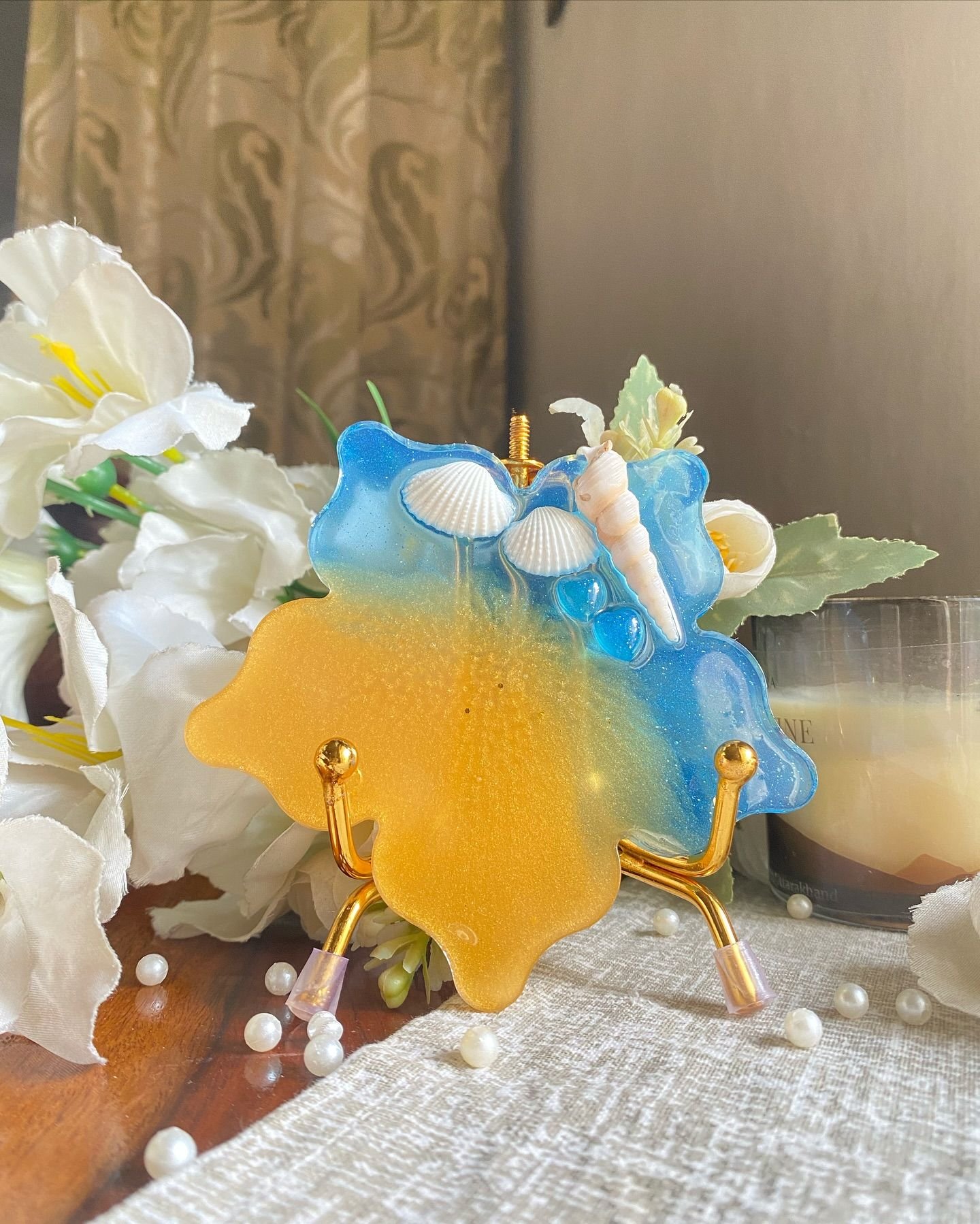 The same coaster stood upright, showing the shells and the graduation of blue into yellow, with white flowers and scattered pearls behind