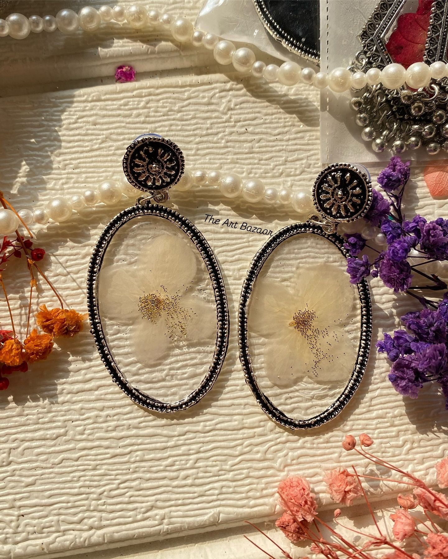 A pair of white resin jhumkas set with a pressed flower